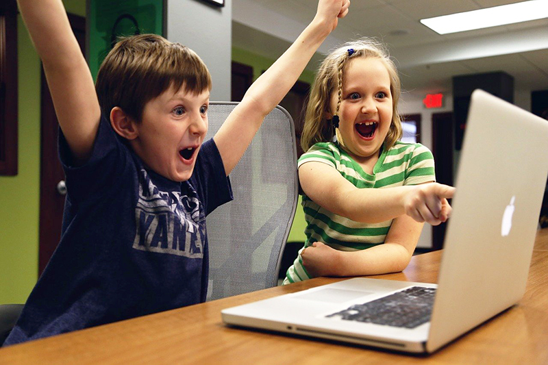 Two children celebrate success at using a laptop