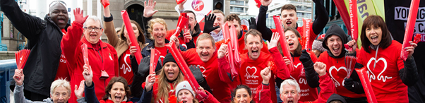 A group of BHF volunteers cheering and raising their arms while wearing BHF t-shirts.