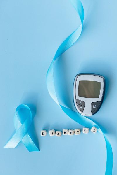 A photograph of a blue ribbon, a glucometer and small blocks spelling the word &#039;diabetes&#039; on a blue table.