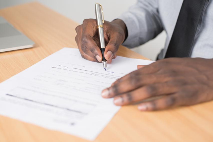 A pair of hands holding a pen, completing a form on a table. 