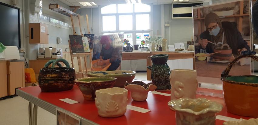 A group of colourful pots assembled on a display table with images of two English for Every Day learners making the pots behind.