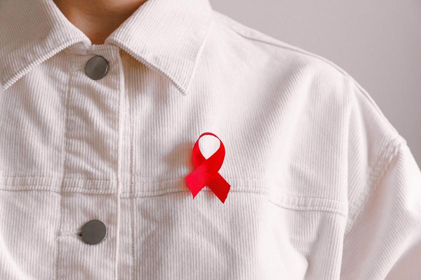 A person wearing a white corduroy jacket with the red HIV awareness ribbon attached to it.