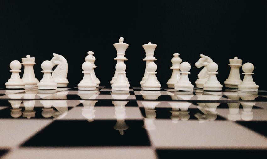 A photograph of white chess pieces on top of a chess board against a black background.