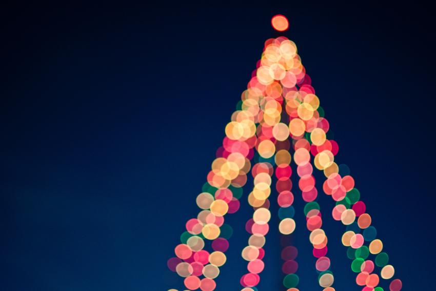 A blurred photograph of Christmas tree lights against a dark blue background.