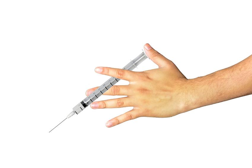 A photograph of a person's hand holding a syringe.