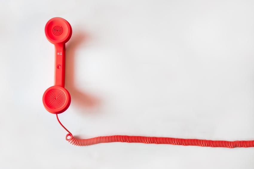 A photograph of a red corded telephone lying flat on a white surface.
